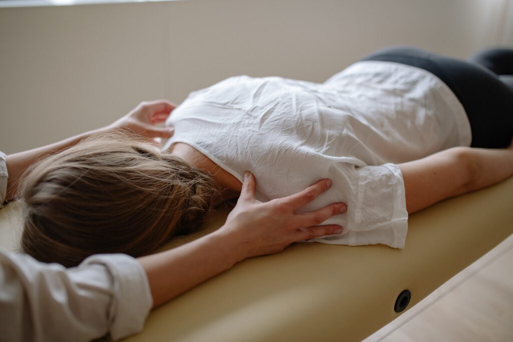 Eine Frau behandelt eine Patientin mit Schmerzen an der Wirbelsäule. Elsa Gomm wendet dafür spezielle Techniken der Osteopathie und Physiotherapie an.